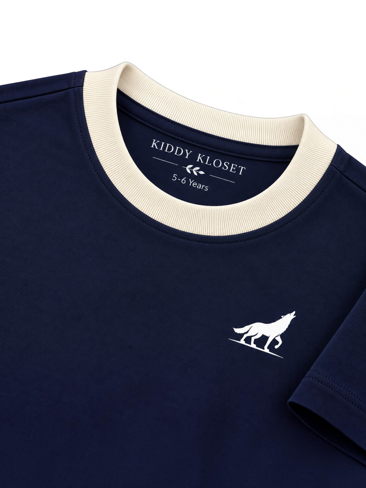 Close up of cream ribbed crew neckline, Kiddy Kloset neck label and white wolf logo on navy tee