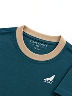 Close up of beige ribbed crew neckline, branded neck print and white wolf logo on teal tee