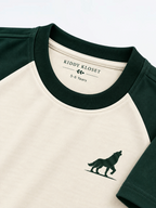 Close up of green ribbed crew neckline and green wolf logo on cream raglan tee