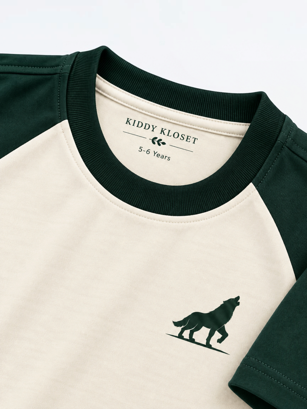 Close up of green ribbed crew neckline and green wolf logo on cream raglan tee