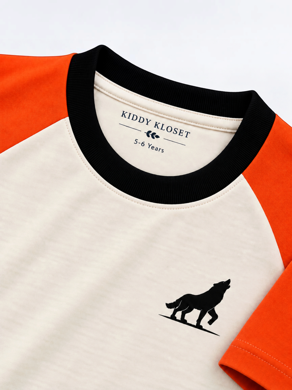 Close up of black ribbed crew neckline, branded neck label and black wolf logo on cream and orange raglan tee
