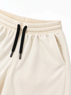 Close up of ribbed waistband, black drawcord and side pocket on kids cream shorts