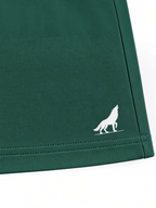 Close up of white wolf logo and stitched hem on kids forest green shorts