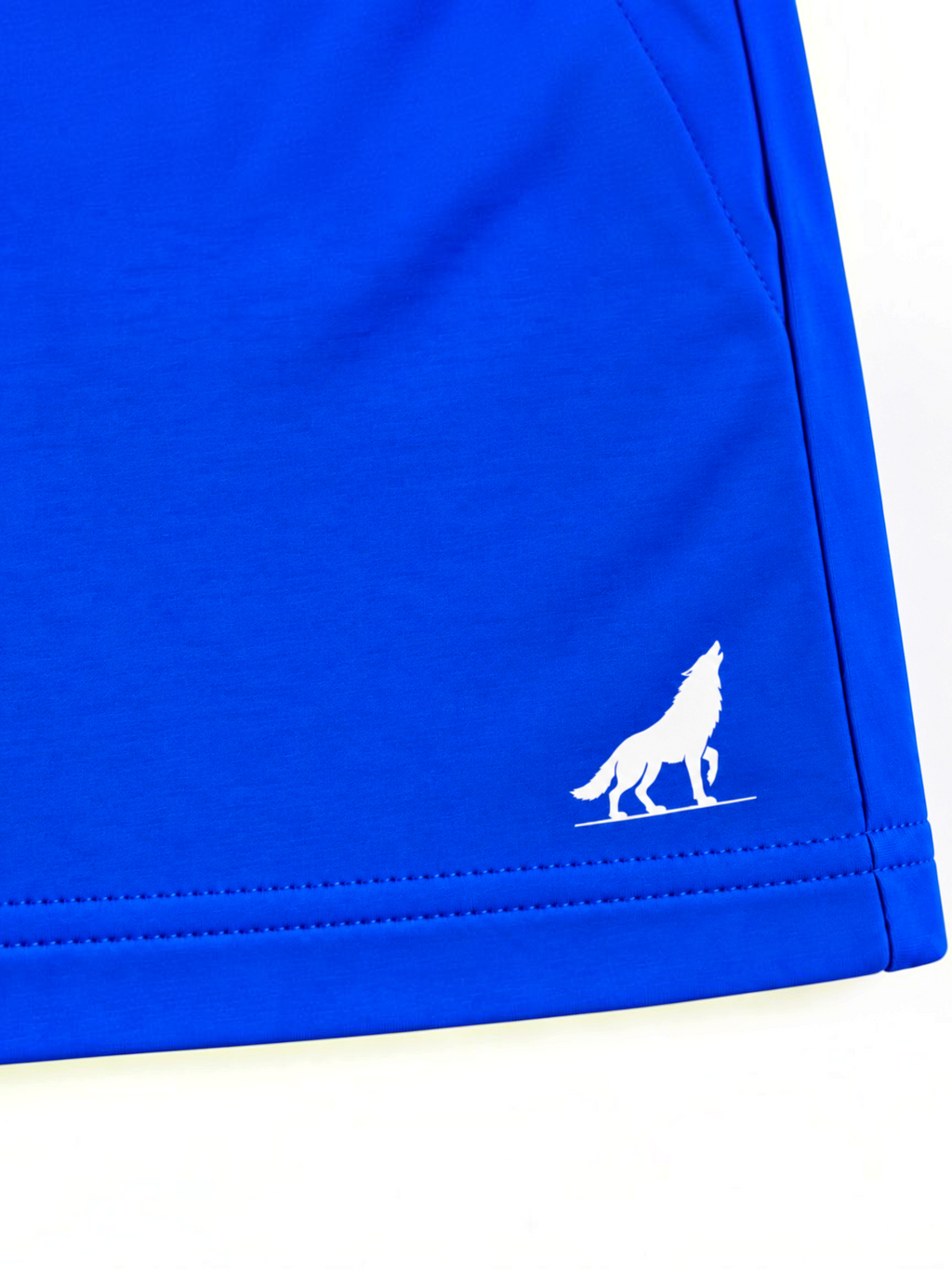 Close up of white wolf logo and stitched hem on kids royal blue shorts